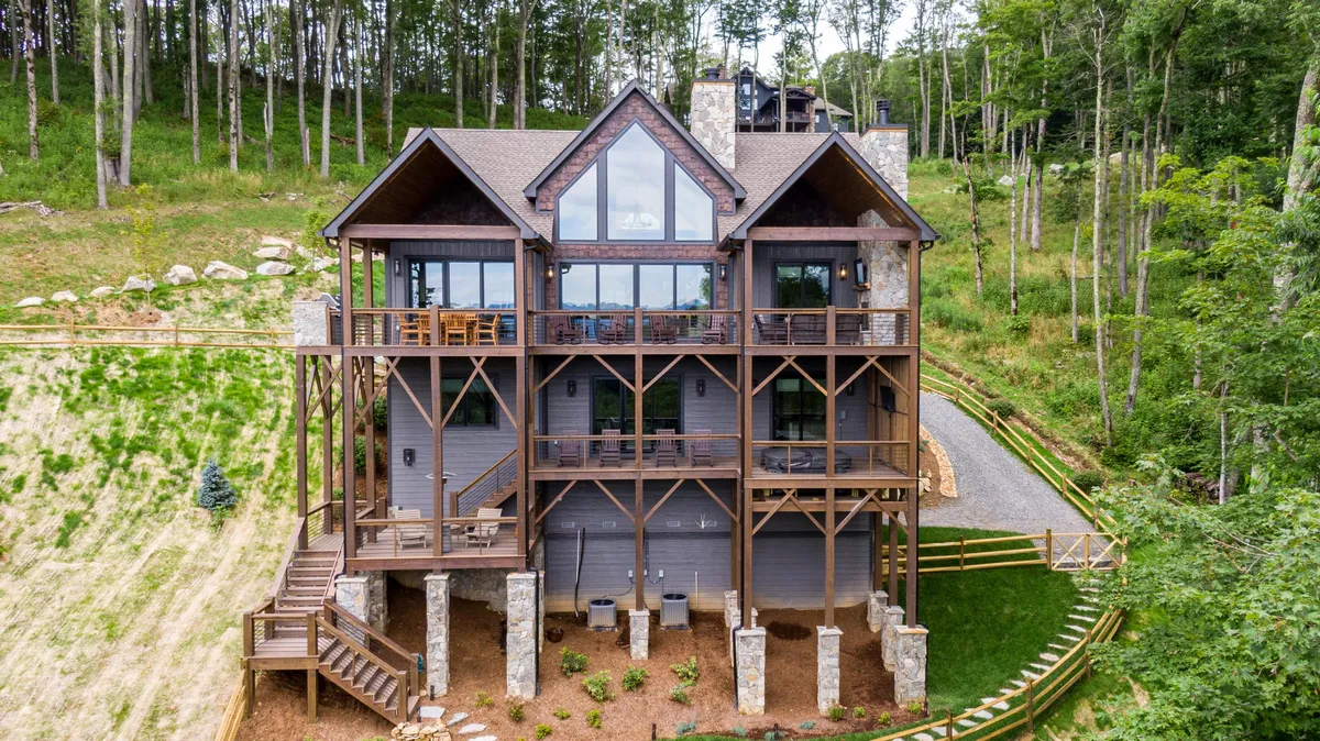 A wide shot of the lodge’s exterior with large windows, a spacious deck, and lush greenery, suggesting ample space for outdoor games, gatherings, and enjoying the natural setting.