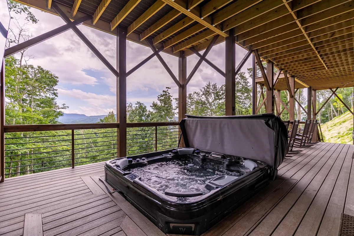 This image highlights a wooden deck with a bubbling hot tub overlooking a serene natural backdrop. The scenic view, surrounded by trees and mountains, invites relaxation and celebration of the outdoors.