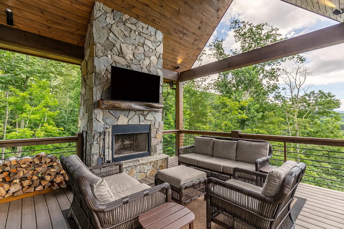 A covered outdoor living space featuring a stone fireplace, comfortable seating, and views of natural greenery. The setting is intimate and cozy, ideal for cool evenings and fire-side chats with friends or family.