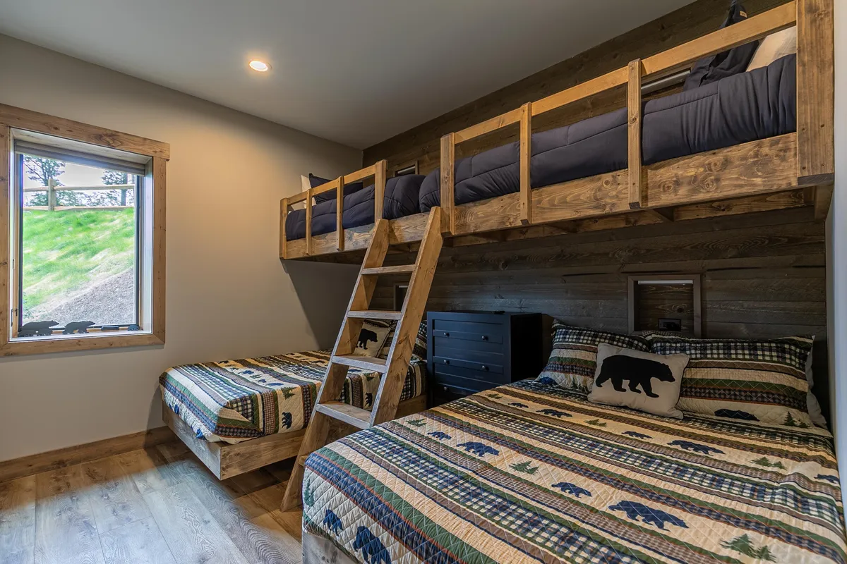 A charming bunkroom setup with multiple bunk beds, each outfitted with cozy decorative pillows and wooden furniture. The space feels playful yet restful, with a window that lets in natural light and invites family bonding, storytelling, or group sleepovers.