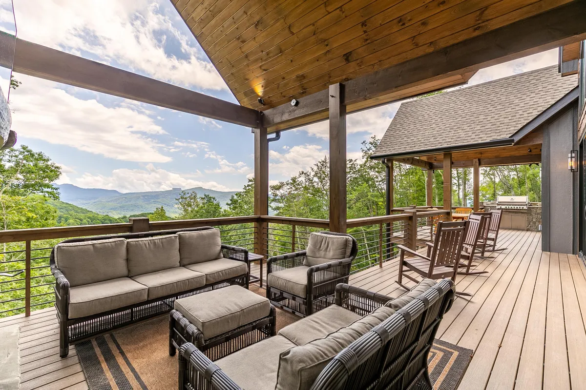 A spacious outdoor deck with comfortable seating, a wooden ceiling, and a railing overlooking a sweeping mountain vista. The furniture is arranged to invite relaxation and socializing while enjoying the view. The deck appears expansive, echoing the description of over 1,250 sq. ft. of outdoor space.