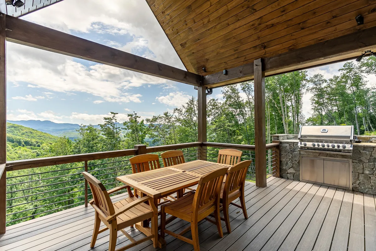A beautiful outdoor deck with a wooden dining set, built-in grill, and breathtaking mountain views. The scene invites outdoor meals, socializing, and relaxation, with the scenic backdrop elevating the alfresco experience.