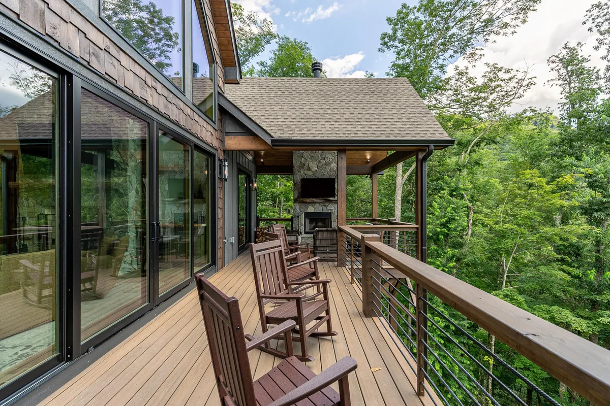 A welcoming outdoor area with wooden rocking chairs positioned near a stone fireplace and expansive glass windows, all nestled amidst lush greenery. This setup offers a comfortable space for guests and pets to unwind while enjoying the outdoors.