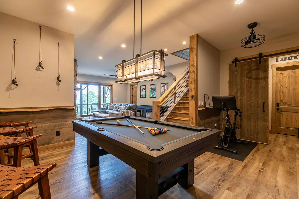 An inviting recreation room featuring a pool table, comfortable sofa area, and stairs, perfect for unwinding after an active day. The space is well-lit and designed for socializing and friendly competition.