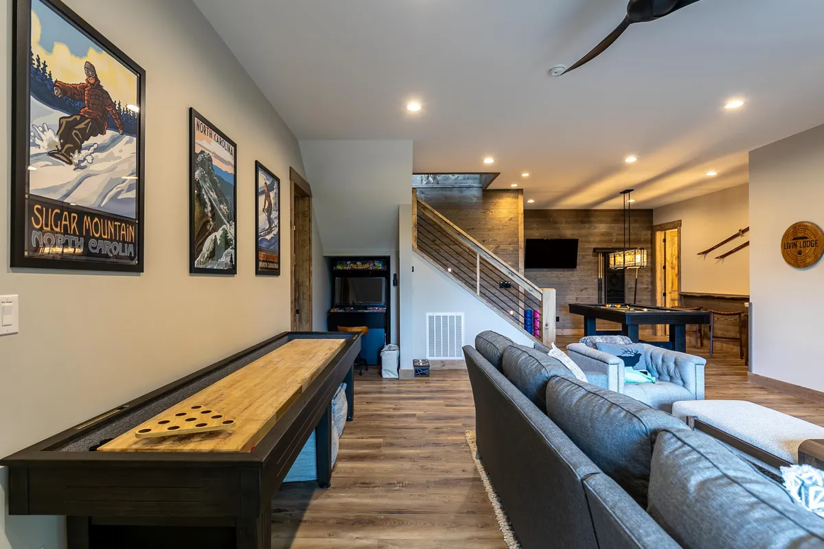 A casual, friendly game area is spotlighted here, featuring a shuffleboard table, sliding staircase, and seating area with TV. Artwork on the wall adds warmth, and the layout encourages social interaction and family fun.